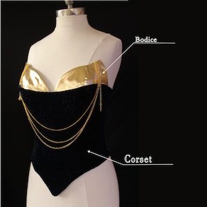 Puede incluir: Un corsé de terciopelo negro con corpiño dorado y detalles de cadena dorada. El corsé se exhibe en un maniquí, mostrando su forma y diseño. Los detalles dorados contrastan con la tela oscura.