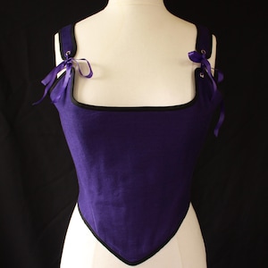 May include: A purple corset with black trim and purple ribbon ties. The corset is on a white dress form.