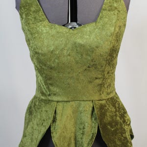 Puede incluir: Un top verde sin mangas de terciopelo con un dobladillo puntiagudo en forma de hoja. El top tiene un escote redondo y un corpiño ajustado.