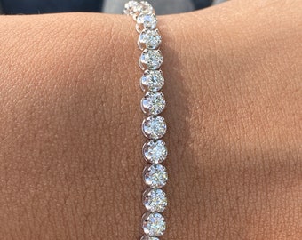 Puede incluir: Un brazalete de tenis de plata con una fila de diamantes redondos y transparentes.