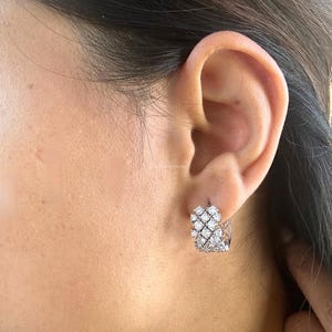 Puede incluir: Pendientes de aro de plata con un racimo de peque&ntilde;as piedras de circonita c&uacute;bica transparentes. Los pendientes se llevan en la oreja de una persona.