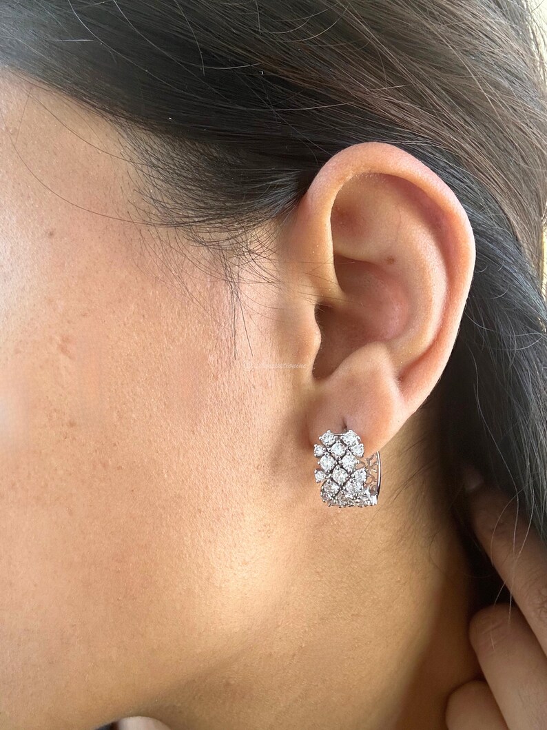 Puede incluir: Pendientes de aro de plata con un racimo de peque&ntilde;as piedras de circonita c&uacute;bica transparentes. Los pendientes se llevan en la oreja de una persona.