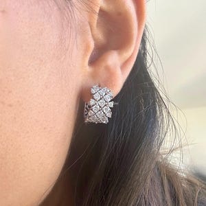 Puede incluir: Un par de pendientes de aro de plata con un racimo de peque&ntilde;as piedras de circonita c&uacute;bica transparentes. Los pendientes est&aacute;n dise&ntilde;ados en un estilo en capas y en cascada.