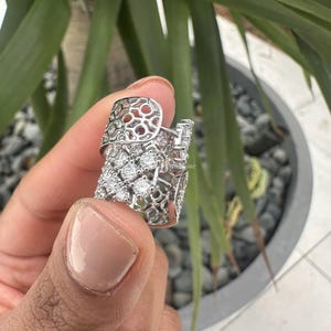 Puede incluir: Un anillo de plata con un dise&ntilde;o delicado e intrincado que presenta un patr&oacute;n de celos&iacute;a y piedras transparentes brillantes.