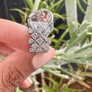 Puede incluir: Un anillo de plata con un grupo de peque&ntilde;os diamantes engastados en un patr&oacute;n geom&eacute;trico. El anillo se lleva en un dedo y el fondo est&aacute; desenfocado.