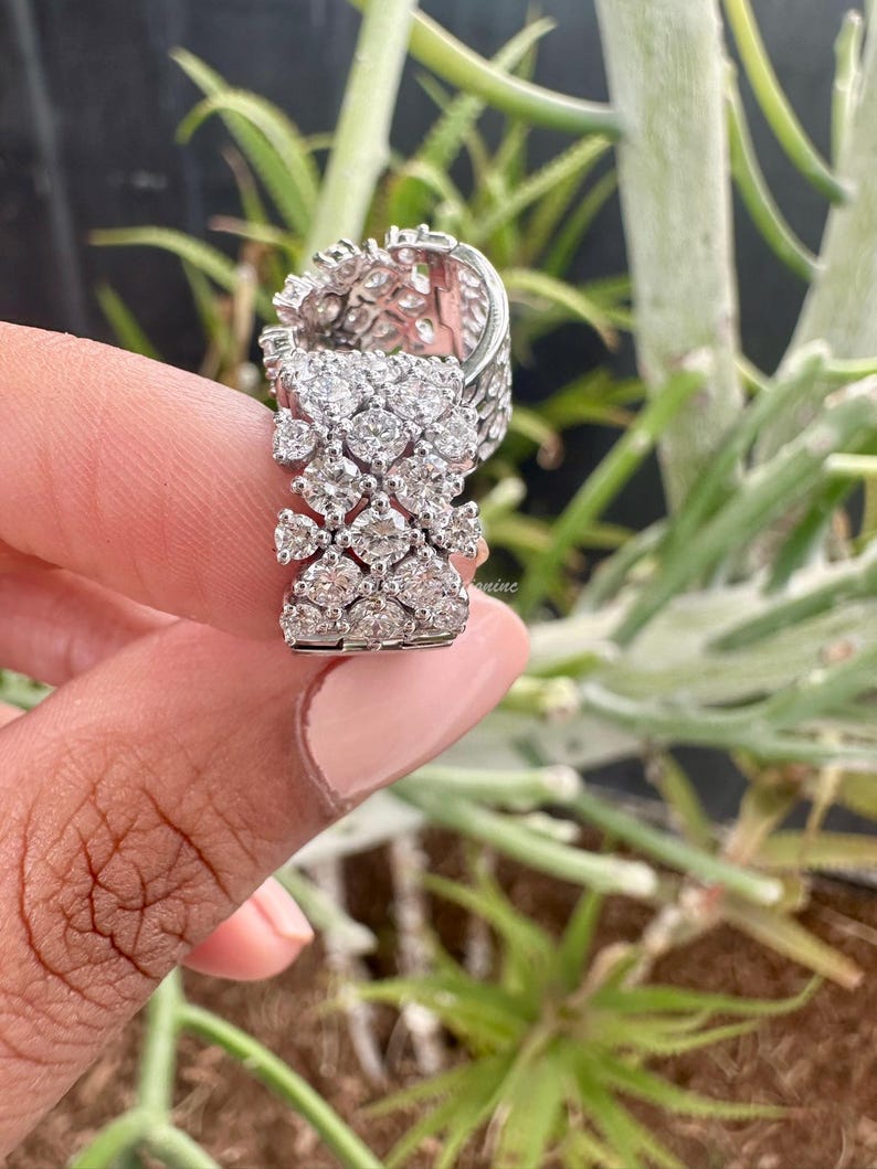 Puede incluir: Un anillo de plata con un grupo de peque&ntilde;os diamantes engastados en un patr&oacute;n geom&eacute;trico. El anillo se lleva en un dedo y el fondo est&aacute; desenfocado.