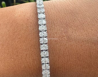 Puede incluir: Un brazalete de tenis de plata con una fila de diamantes de forma ovalada.