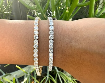 Puede incluir: Dos pulseras de tenis con una fila de piedras de circonita cúbica transparentes. Las pulseras son de 9 quilates y se muestran en la muñeca de una persona.