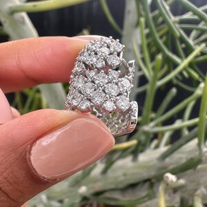 Puede incluir: Un anillo de plata con un gran racimo de diamantes brillantes engastados en un dise&ntilde;o delicado e intrincado.