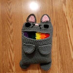 May include: Gray crocheted cat-shaped stuffed toy with rainbow yarn peeking out of its mouth.