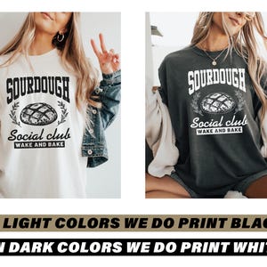 May include: Two t-shirts with a sourdough bread design. The white t-shirt has black text and the dark grey t-shirt has white text. Both shirts say "Sourdough Social Club Wake and Bake".