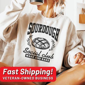 May include: A white sweatshirt with the text "Sourdough Social Club Wake and Bake" and a graphic of a sourdough bread loaf.