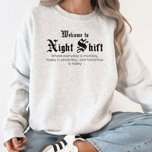May include: A light gray sweatshirt with the text "Welcome to Night Shift" in a gothic font. Below the title is the quote: "Where everyday is monday, today is yesterday, and tomorrow is today."