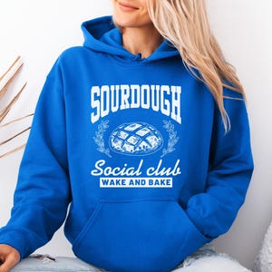May include: A royal blue hoodie with a white graphic of a sourdough bread loaf and the text "Sourdough Social Club Wake and Bake".