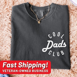 May include: A dark gray t-shirt with a white circle graphic that says "Cool Dad's Club".