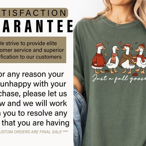 Peut inclure: T-shirt vert olive avec une illustration de quatre oies v&ecirc;tues de tenues d'automne, notamment des pulls, des &eacute;charpes et des chapeaux. Le texte "Just a fall goose" est &eacute;crit en dessous.