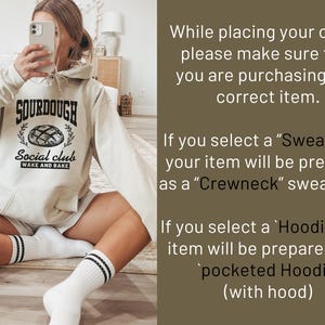 May include: A woman wearing a light beige hoodie with the text "SOURDOUGH Social club WAKE AND BAKE" and a graphic of a loaf of bread. The hoodie has a drawstring hood.