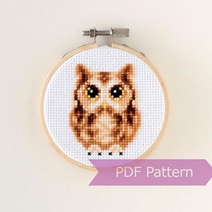 May include: A brown and white owl cross stitch pattern in a wooden embroidery hoop. The pattern is for a PDF download.