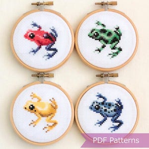 Puede incluir: Cuatro aros de bordado de punto de cruz con diseños de ranas coloridas. Cada rana es de un color diferente: rojo, verde, amarillo y azul. El texto "PDF Patterns" es visible en una pancarta.