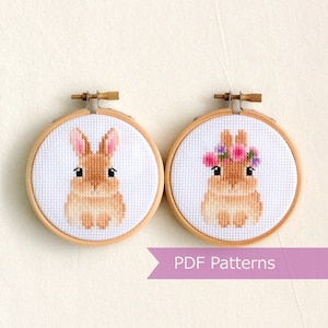 May include: Two embroidery hoop patterns featuring a brown bunny. One bunny is wearing a flower crown. The text "PDF Patterns" is on a purple banner.