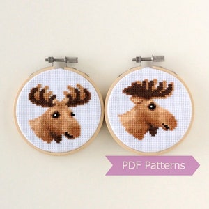 May include: Two brown moose cross-stitch patterns in round wooden embroidery hoops. The patterns are ready to be stitched and are available as PDF downloads.  PDF Patterns.
