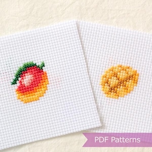 May include: Two square pieces of white Aida fabric featuring cross-stitch designs. One piece displays a gradient peach with a green leaf, while the other shows a textured yellow circular fruit. A purple banner with the text PDF Patterns is visible.