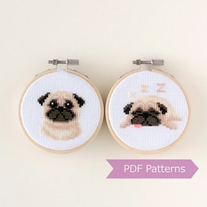 May include: Two cross-stitch patterns of pugs in embroidery hoops. The first pattern shows a pug looking straight ahead, and the second pattern shows a pug sleeping with its tongue sticking out. The text "PDF Patterns" is printed on a purple ribbon.