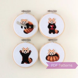 Puede incluir: Cuatro patrones de bordado en forma de aro que representan pandas rojos en diferentes poses. Los patrones están impresos en tela blanca y están listos para ser bordados. Los aros son de madera y tienen un acabado natural. El texto "PDF Patterns" está impreso en una cinta morada.