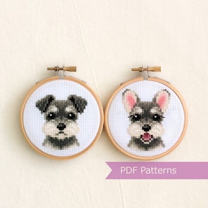 May include: Two miniature cross-stitch embroidery hoops featuring images of a miniature schnauzer dog. The dog in the left hoop has a serious expression, while the dog in the right hoop has a happy expression. The text "PDF Patterns" is printed on a purple banner below the hoops.