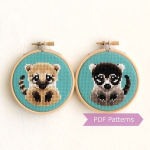 Peut inclure: Deux broderies en forme de cerceau pour accrocher au mur, avec des motifs de raton laveur et de coati en point de croix. Les cerceaux sont en bois avec une finition brun clair et le tissu est bleu turquoise clair.