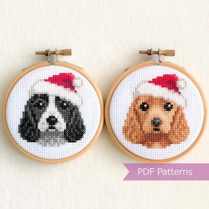 May include: Two cross-stitch patterns of dogs wearing Santa hats. The patterns are in embroidery hoops and are ready to be stitched.