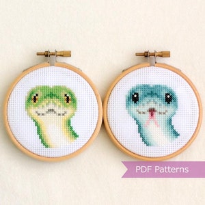 May include: Two embroidery hoop patterns featuring cute cartoon snakes. The snake on the left is green with yellow accents and the snake on the right is blue with pink accents.  PDF Patterns.