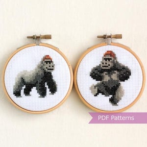 May include: Two cross-stitch embroidery hoops featuring gorilla designs. The gorillas are in shades of gray and black, wearing red hats. The hoops are mounted in wooden frames. The text "PDF Patterns" is visible.