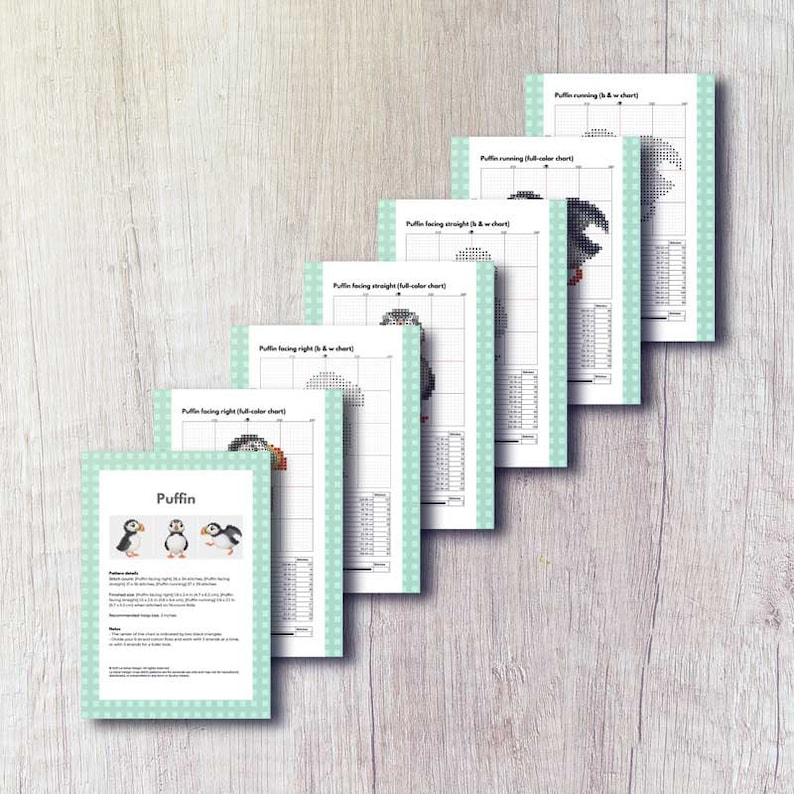 May include: A stack of cross-stitch pattern charts featuring puffins. The charts show different poses of the bird, including running and facing straight. The charts are printed on white paper with a light green border and are arranged on a light wood surface.