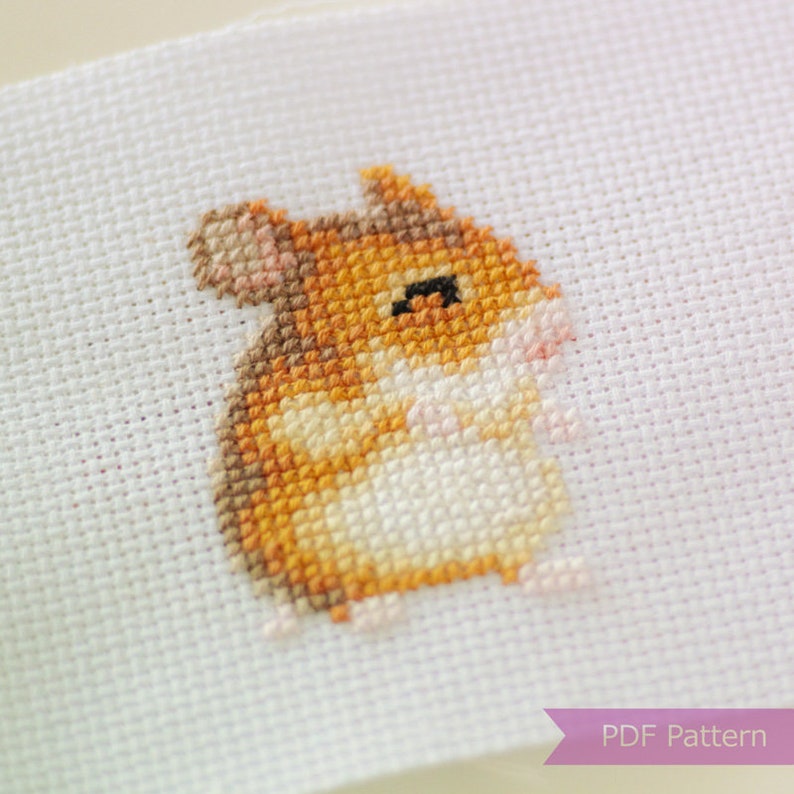 May include: Cross stitch pattern of a small, brown hamster with white markings. The hamster is sitting on a white background. The pattern is labeled "PDF Pattern".