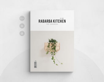May include: A cookbook titled Rabarba Kitchen The Cookbook with a white top section and a light grey bottom section. The cover features a small wooden crate containing a trailing green ivy plant and a barcode in the bottom left corner.