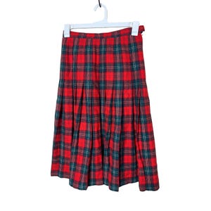 Puede incluir: Falda a cuadros rojos, verdes y blancos colgada de una percha blanca. La falda es plisada y tiene una longitud midi. El estampado de cuadros es un diseño clásico, adecuado para diversas ocasiones.