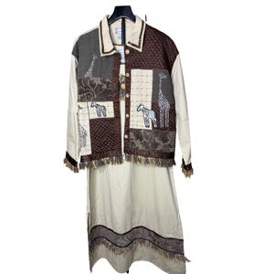 May include: A two-piece safari-themed outfit featuring a jacket and a dress. The jacket has a patchwork design with embroidered zebras and giraffes, and a fringe trim. The dress is a solid beige color with a matching fringe trim at the hem.