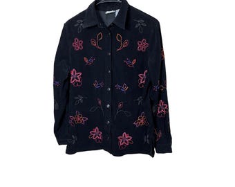 May include: Black corduroy button-down shirt with embroidered floral and leaf designs in pink, orange, and blue. The long-sleeved shirt has a collar and is hanging on a black hanger.