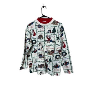 May include: White long-sleeve shirt with a red collar featuring a Christmas-themed pattern. The pattern includes Santa Claus, Christmas trees, and holiday greetings. The shirt is hanging on a black hanger.