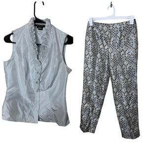 May include: A two-piece women's outfit. The sleeveless top is a light blue with a ruffled collar and button-down front. The pants have a geometric pattern in shades of silver, black, and blue.