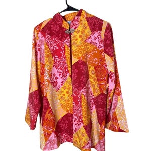 May include: A patchwork blouse with a mandarin collar and long sleeves. The blouse features a vibrant mix of floral and paisley patterns in shades of red, pink, orange, and yellow. A decorative clasp secures the front.