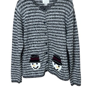 Könnte beinhalten: Ein schwarz-weiß gestreifter Cardigan mit einem Schneemann-Design auf jeder Tasche. Der Cardigan hat einen Knopfverschluss und lange Ärmel.