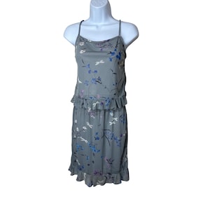 May include: A gray floral print dress with spaghetti straps. The dress features a fitted bodice, a ruffled waist, and a knee-length skirt. The floral pattern includes blue, purple, and white flowers and dragonflies.