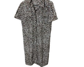 May include: A short-sleeved, button-down dress with a leopard print pattern. The dress is hanging on a black hanger against a white background. The dress has a collared neckline and two small pockets on the chest.