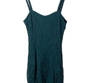 May include: A dark teal lace dress with spaghetti straps hangs on a black hanger. The dress features a fitted bodice and a flared skirt, with a scalloped hemline. The intricate lace pattern covers the entire dress.