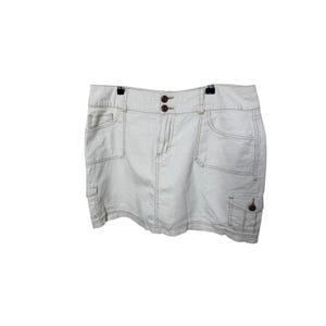 May include: A light beige cargo skirt featuring a waistband with two dark brown buttons, a front zipper closure, two large side pockets, and two smaller flap pockets on the lower front. The garment is constructed with visible tonal stitching.