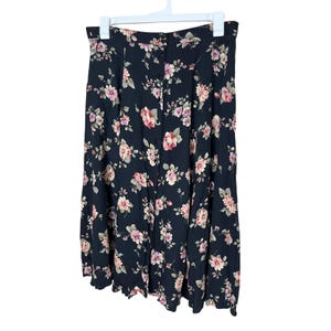 Pode incluir: Saia preta com estampa floral pendurada em um cabide branco. A saia apresenta uma frente com botões e um padrão de flores rosa e brancas. A saia é feita de tecido leve.