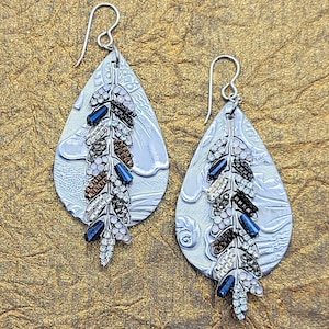 Silver feathers decorated with crystals, metals and glass beads atop genuine leather with patterned silver embellishment, silver hooks