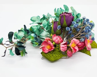 Facinator with purple roses, pink silk blossoms, mini blue flower clusters, and a hanging silk teal delphinium flowers on claw clasp